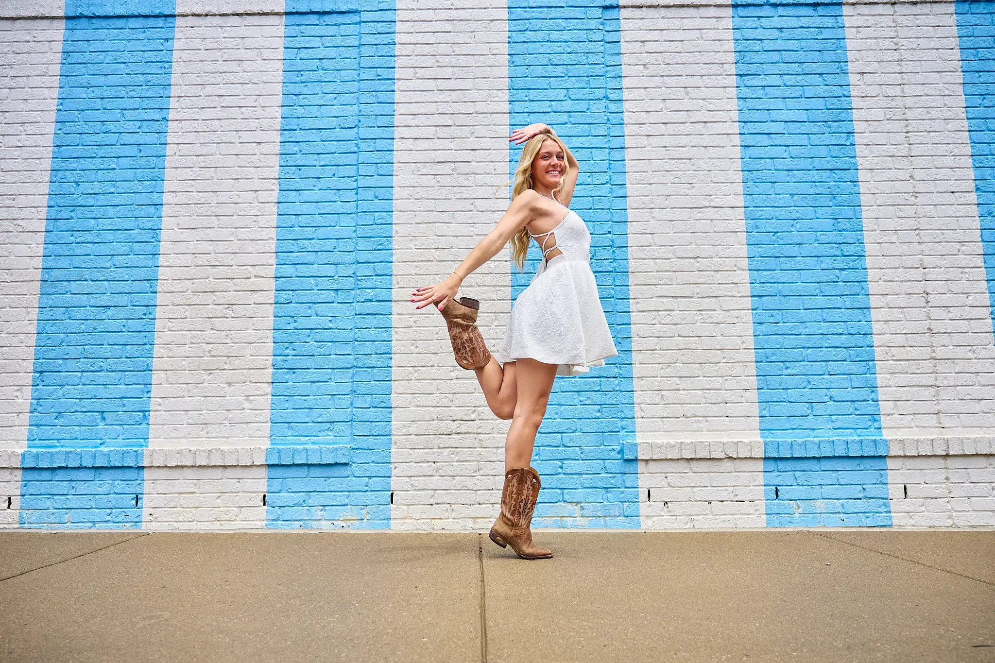 Woman in white dress and cowboy boots against a blue striped Nashville photo wall
