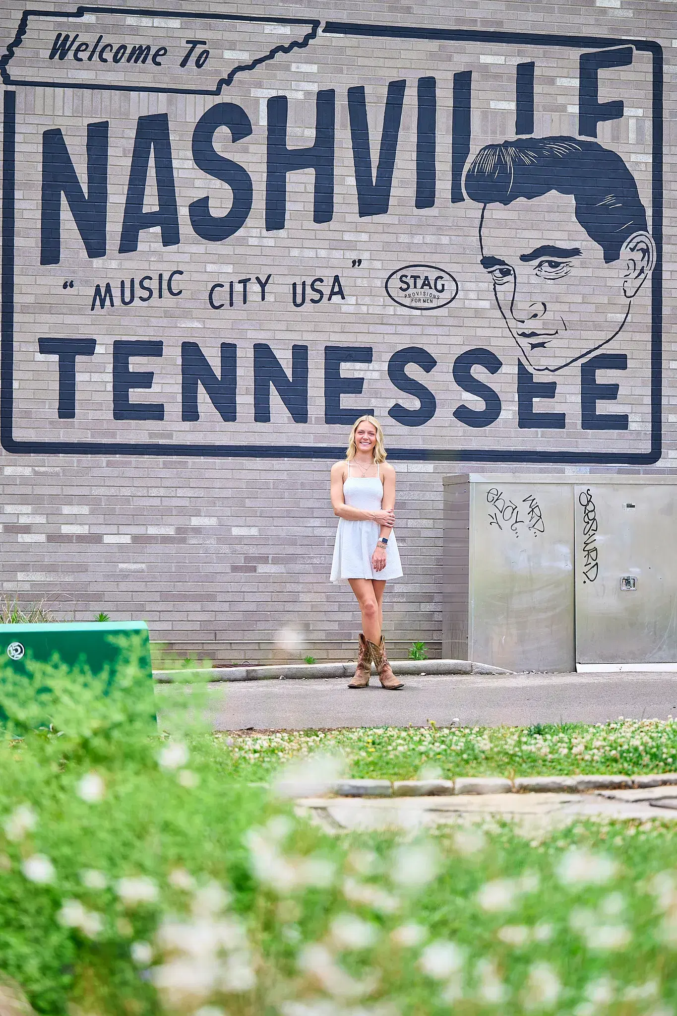 Woman in white dress posing in front of Welcome to Nashville mural